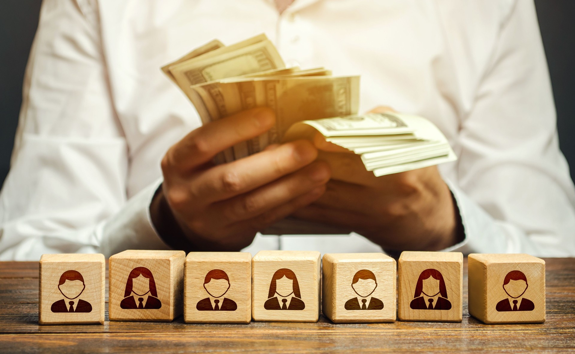 A man is counting money in his hands over blocks with symbols of employees. Wage fund. Accounting and budgeting. Payday. Expanding a profitable business, recruiting and training employees.